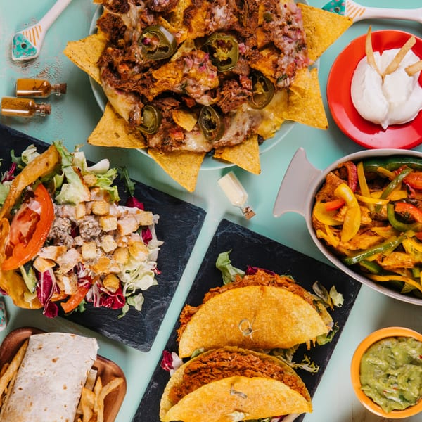 El Castillo Mexicano's nachos, tacos, fajitas, salad, burrito, and guacamole spread on a blue table.