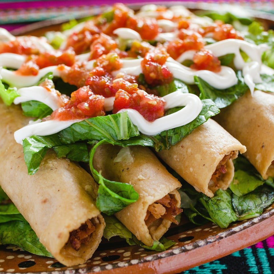 Crispy Mexican taquitos topped with fresh lettuce, salsa, and a drizzle of sour cream.